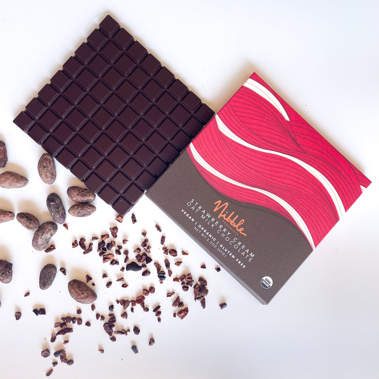 Strawberry Cream Oat Milk Chocolate bar unwrapped with cacao nibs and packaging – Nibble Chocolate