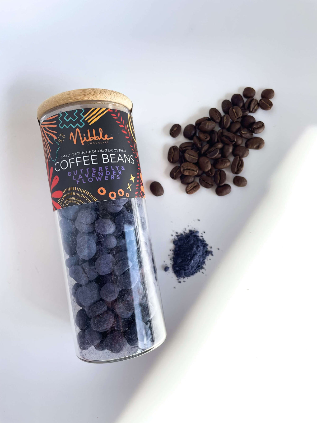 Glass Jar of chocolate-covered coffee beans with butterfly pea and lavender flavor on white background