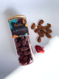 Glass Jar of strawberry-flavored chocolate-covered almonds with pieces scattered on white background