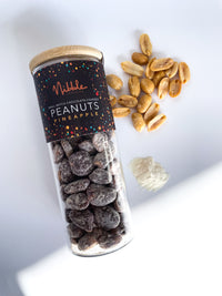 Glass Jar of pineapple chocolate-covered peanuts with scattered pieces on white background