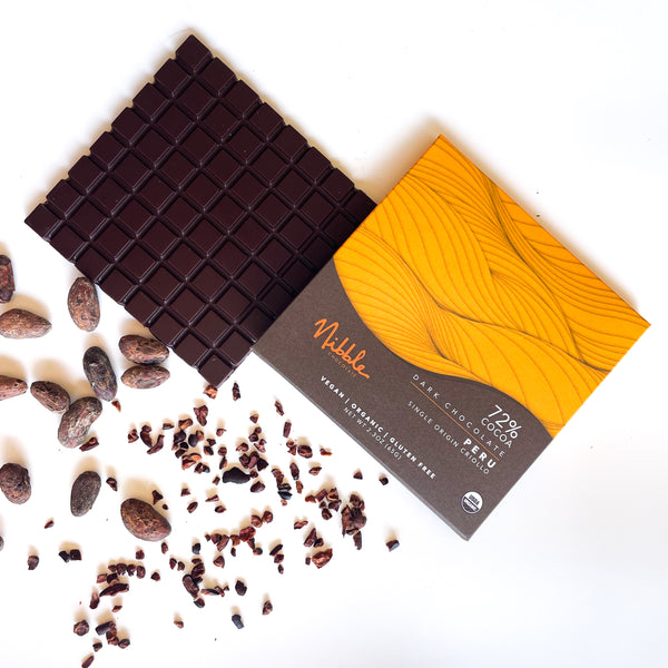 Nibble Chocolate dark chocolate bar with 72% cocoa from Peru, surrounded by cacao nibs and beans.
