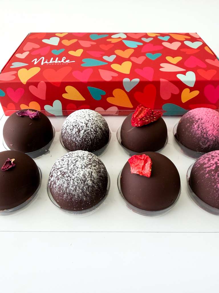 Assorted chocolate truffles in front of a heart-patterned box with 'Niddle' branding.