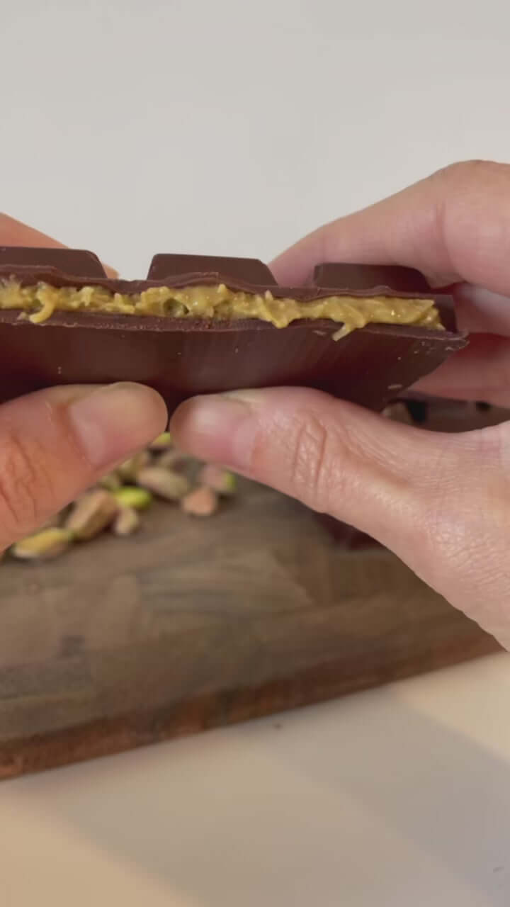 Close-up of hand holding artisan chocolate bar with golden toppings – Dubai chocolate