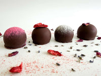 Four chocolate truffles with decorative elements on a white surface