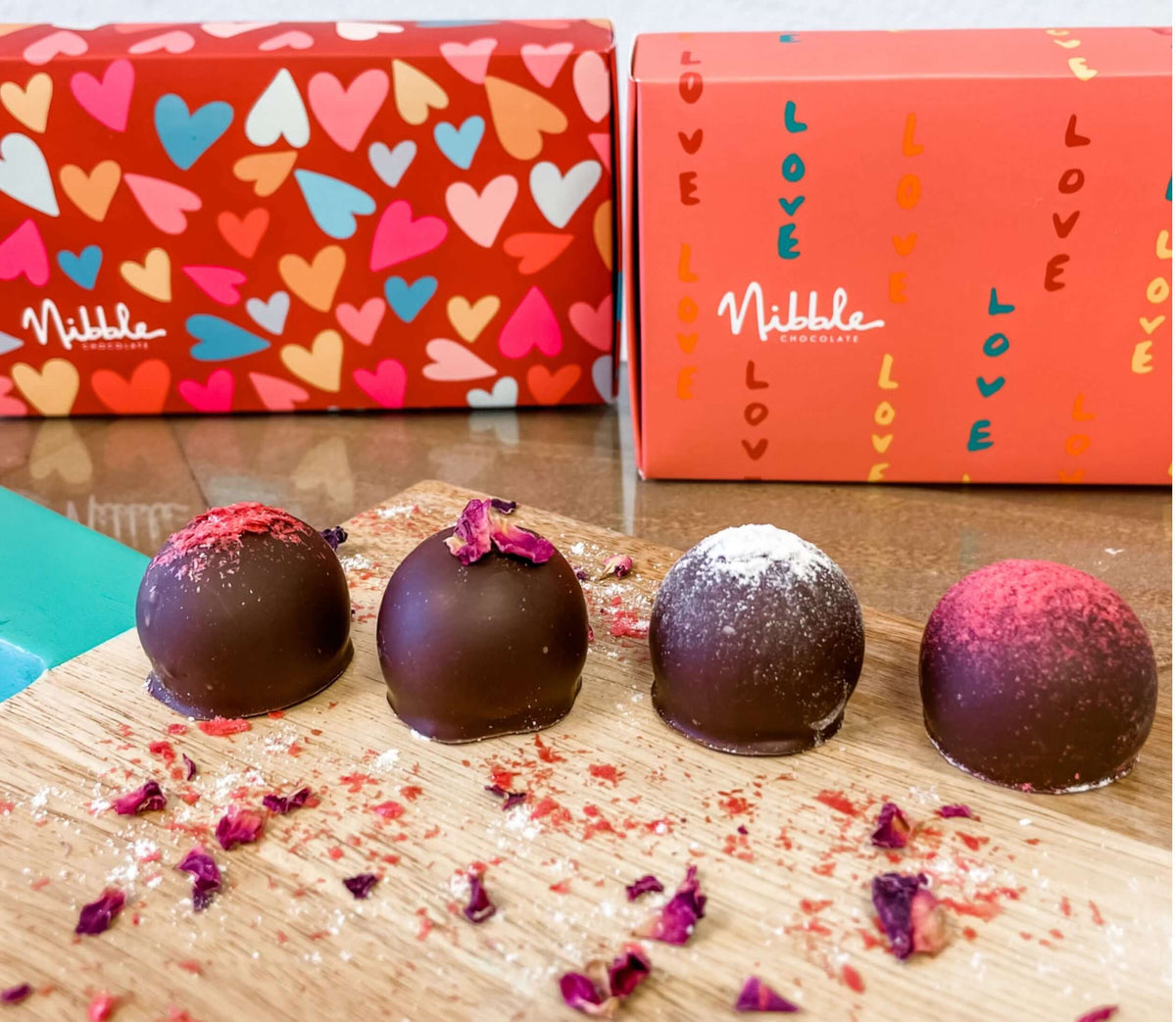 Assorted organic chocolate truffles in front of red Valentine's Day gift box, surrounded by festive sprinkles